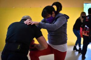 Una mujer joven con pelo oscuro, coleta y sudadera gris practica autodefensa frente a un hombre